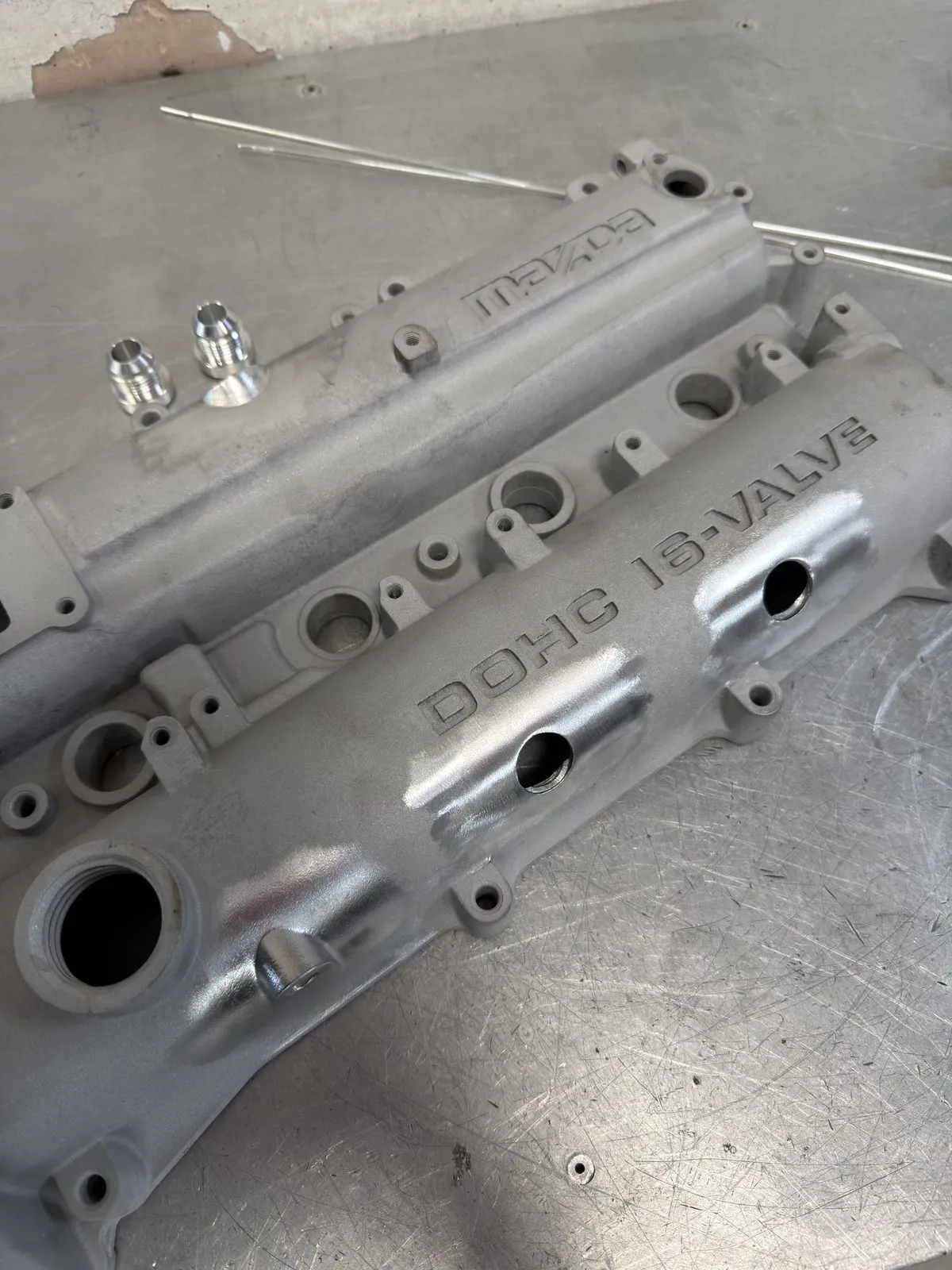 The blasted cover with two ports drilled through the top on the exhaust side and the AN10 weld bungs staged beside it