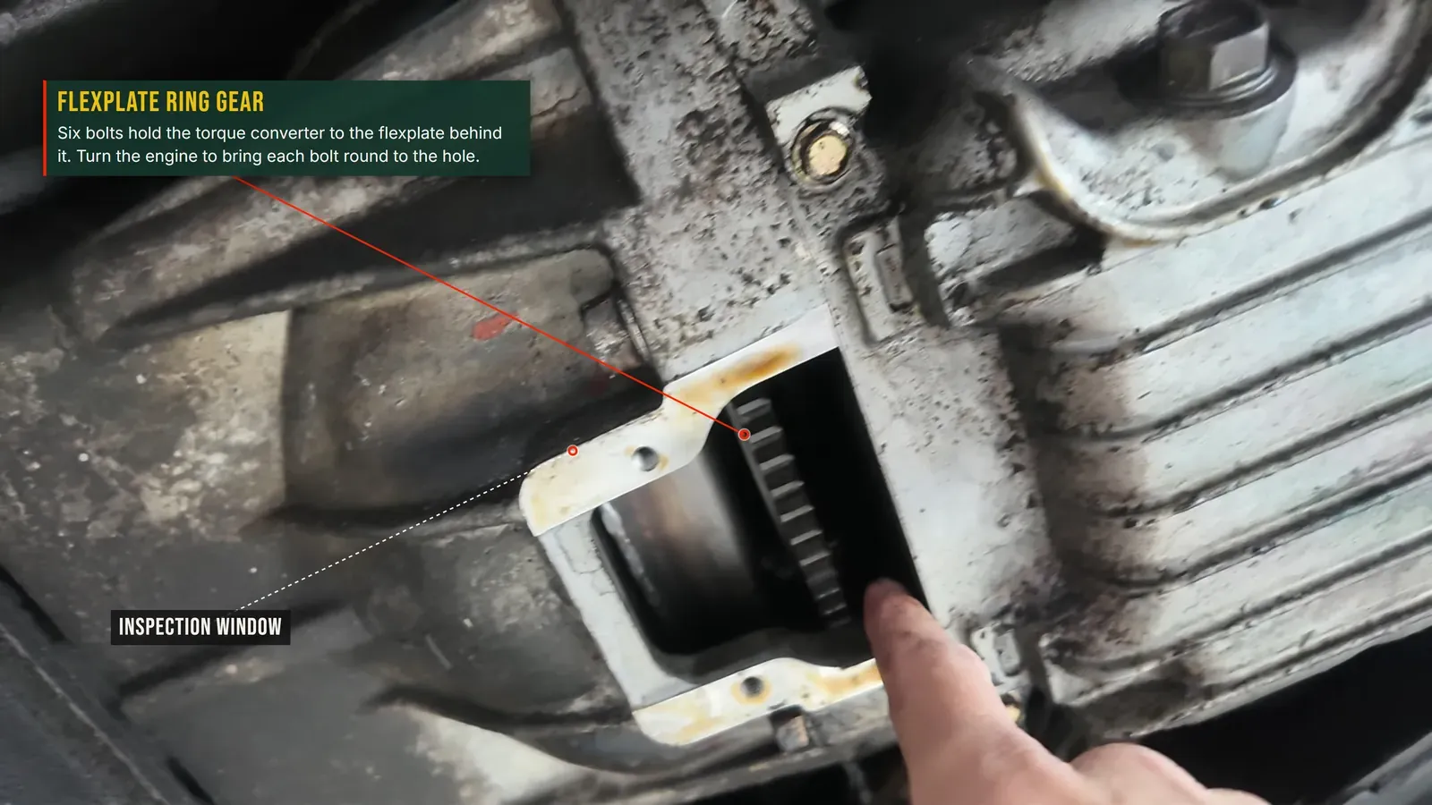 Annotated photo: looking through the bellhousing inspection window at the flexplate ring gear, where the six torque-converter bolts come undone
