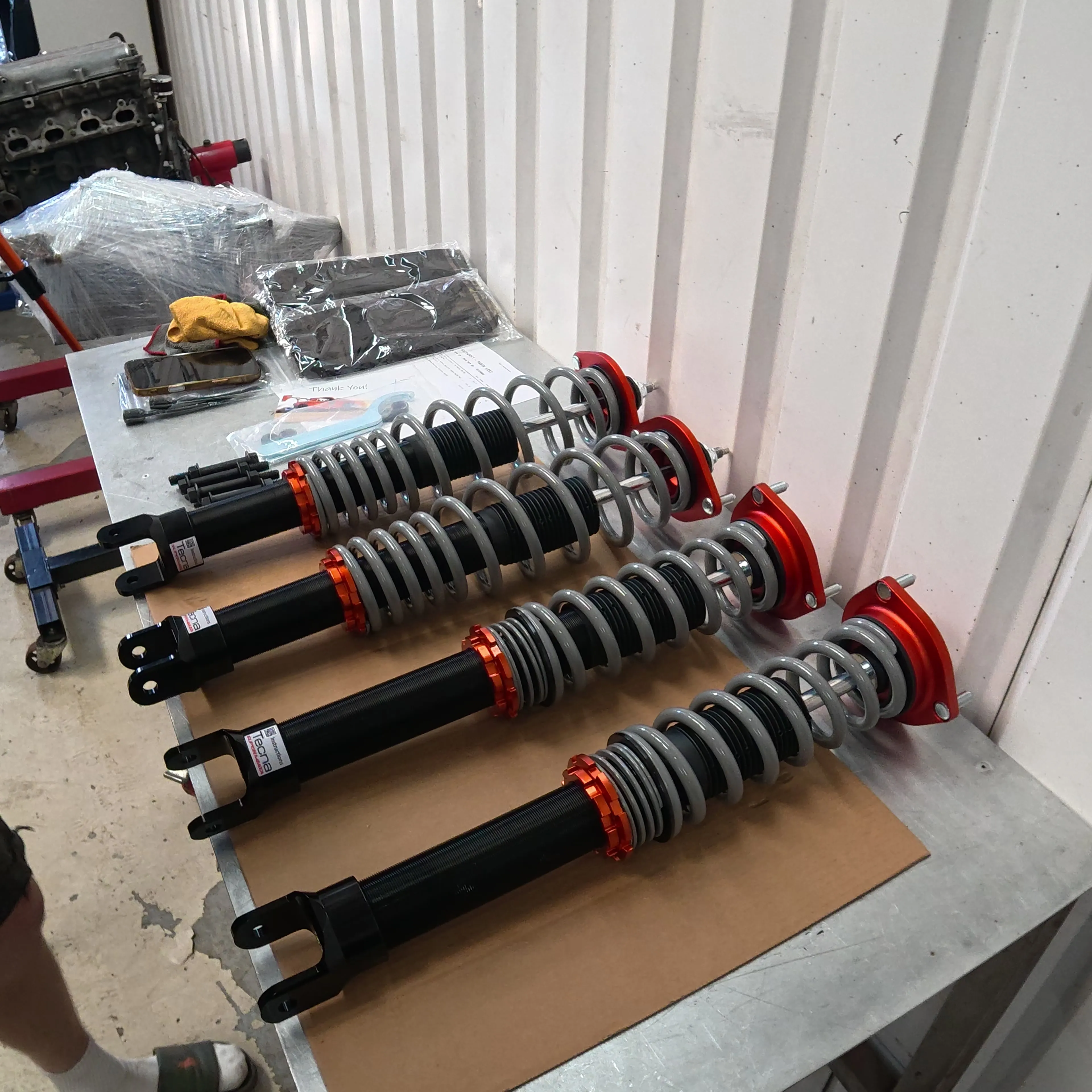 Four assembled Tecna coilovers laid out on cardboard on the workshop bench