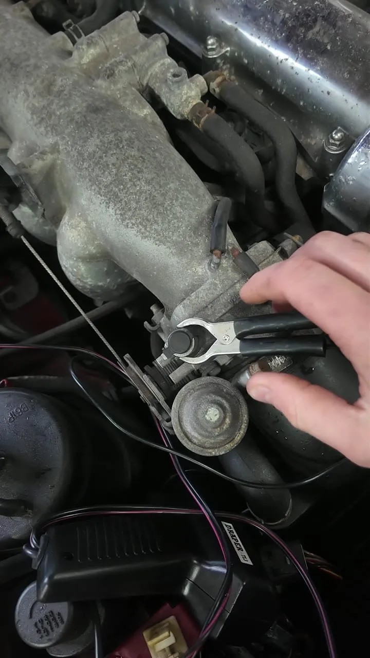 A Mazda MX-5 crank-angle sensor with its slotted adjustment plate, being checked with a timing light