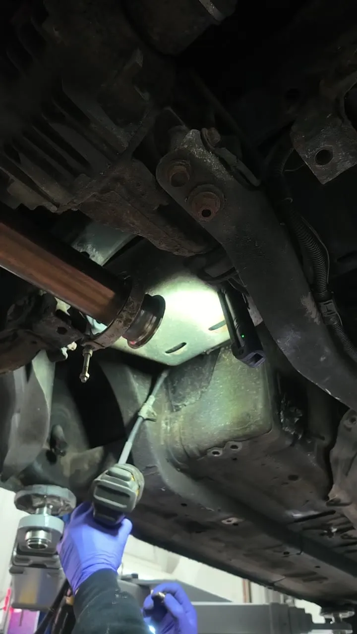 Underbody view dropping the heat shield to reach the MX-5 handbrake cable