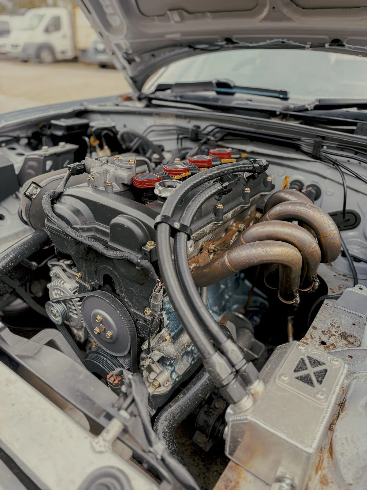A finished black baffled rocker cover fitted in an MX-5 engine bay with braided lines running to the catch can
