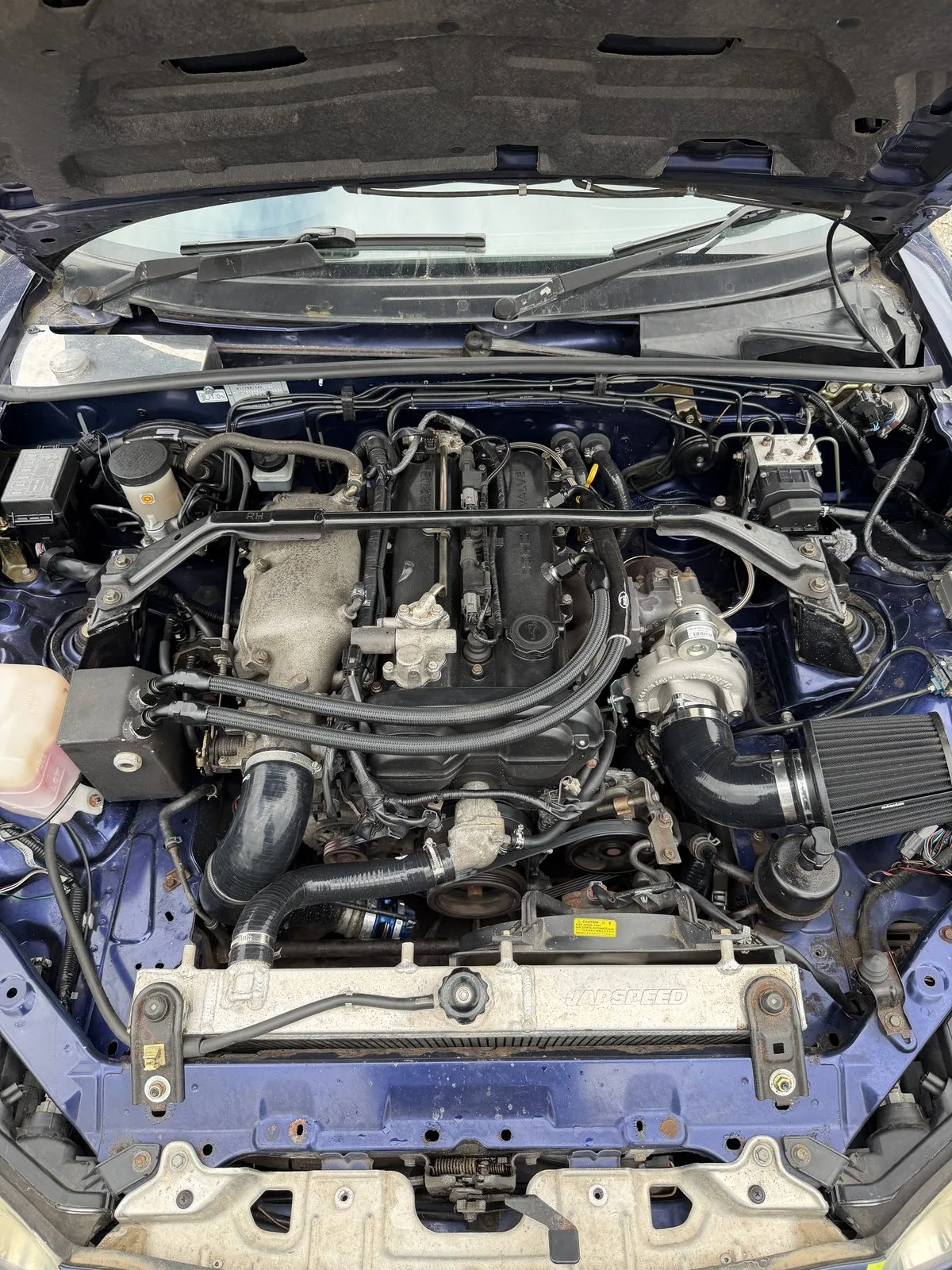 A black baffled rocker cover fitted in a blue turbocharged MX-5 engine bay