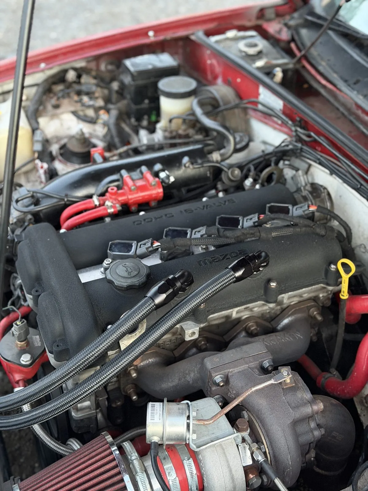A black baffled rocker cover with braided lines off the angled fittings in a red turbocharged MX-5 engine bay
