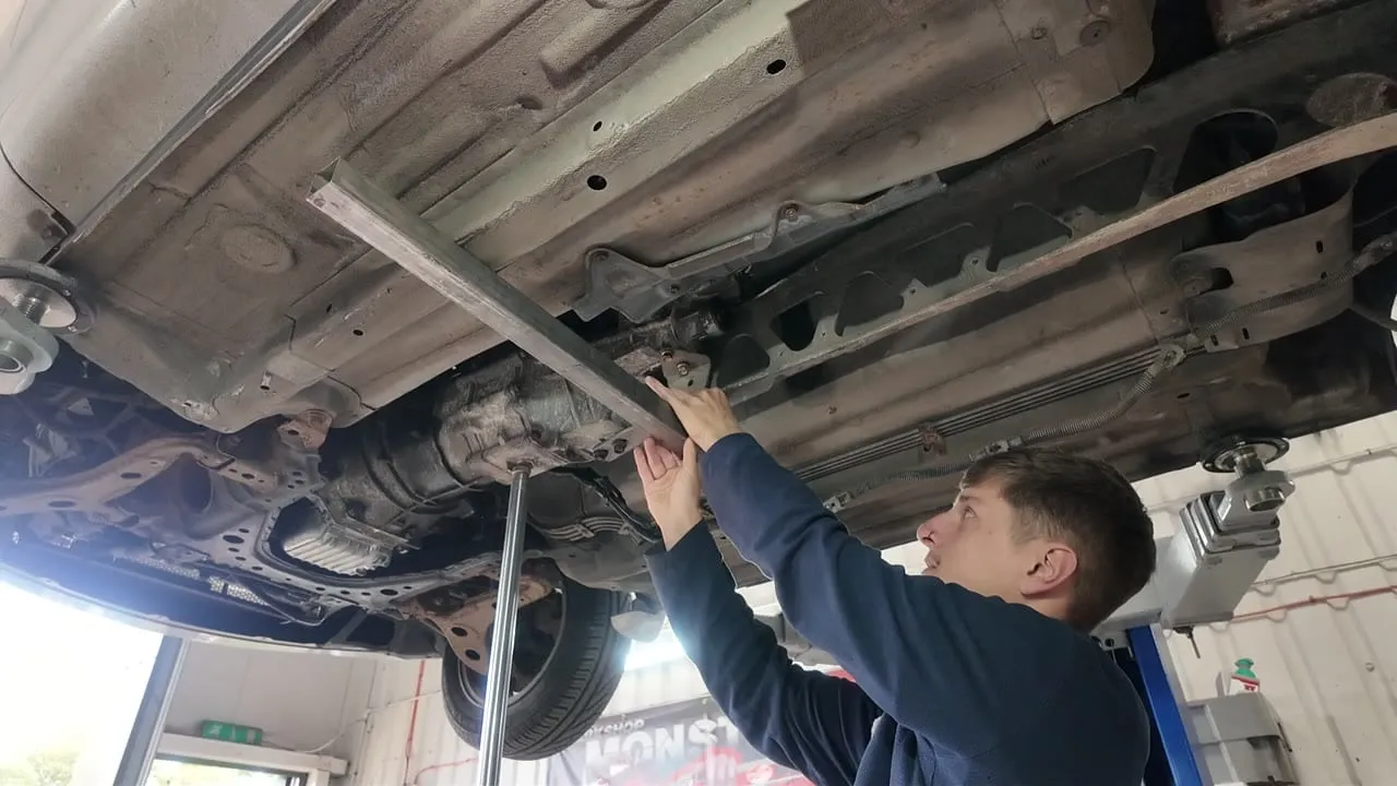 A straight edge laid across the chassis legs to measure up to the Z-bracket bolt head