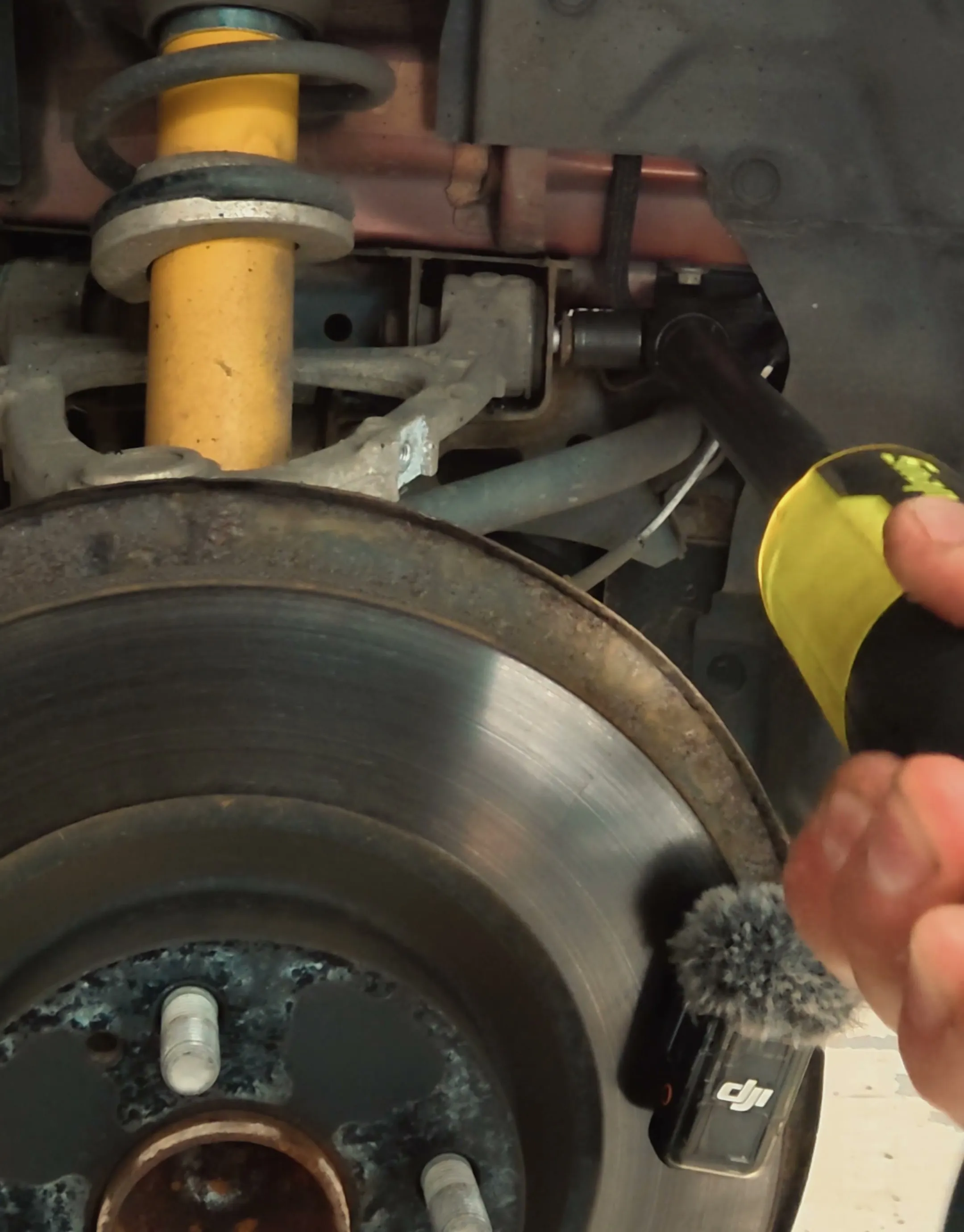Breaker bar on one of the top arm bolts at the subframe mount, with the original damper and brake disc in view