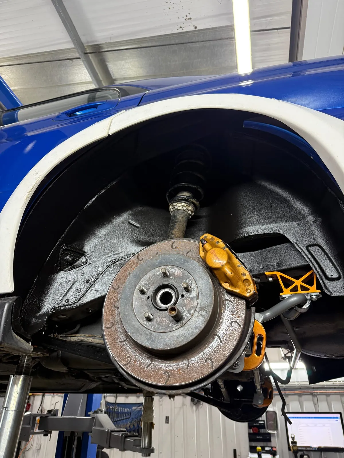 The rebuilt rear corner through the wide arch, sealed inner arch and gold caliper on a grooved disc
