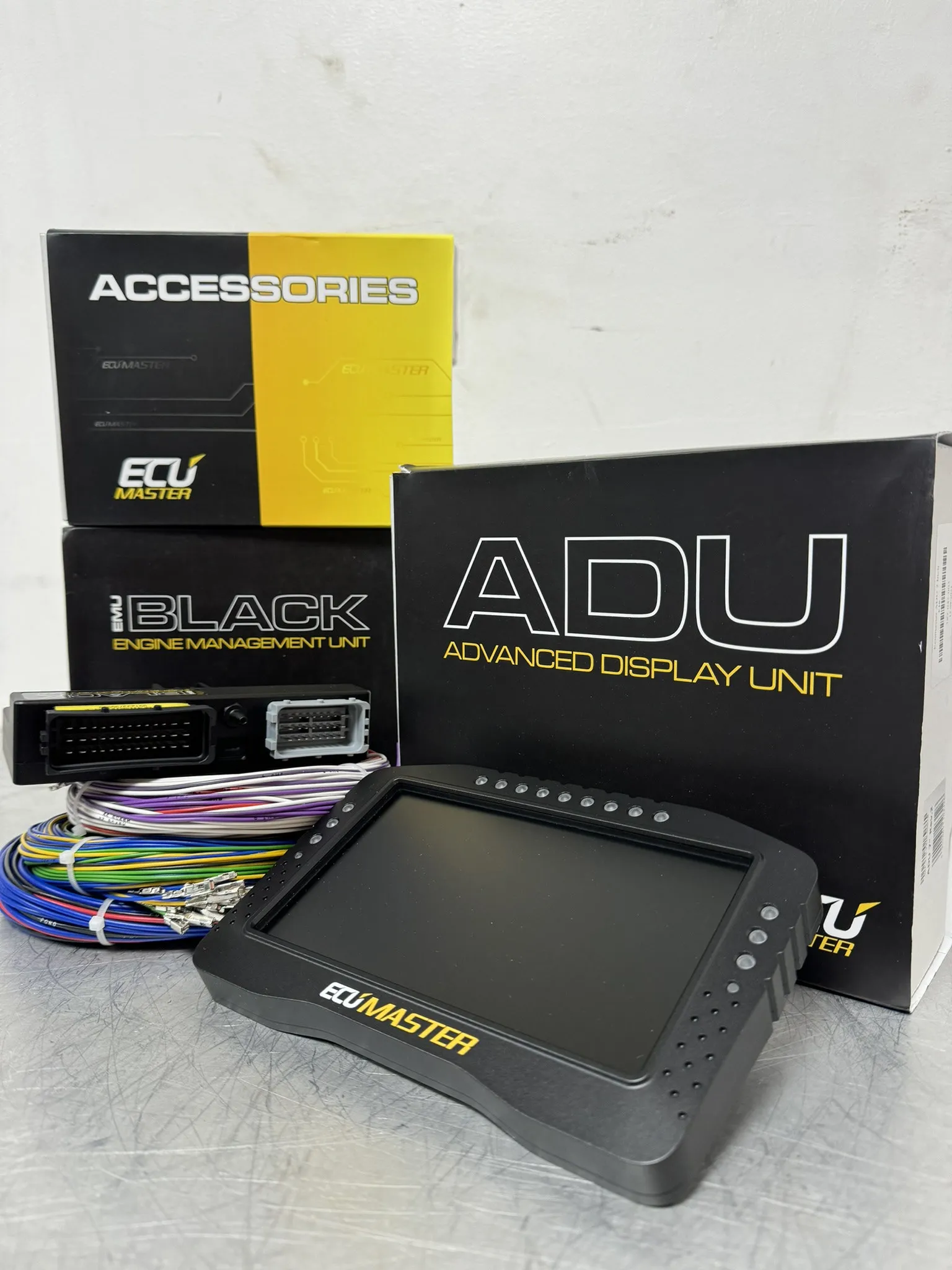 The Ecumaster EMU Black ECU and the ADU advanced display unit, boxed on the bench with the flying lead harness