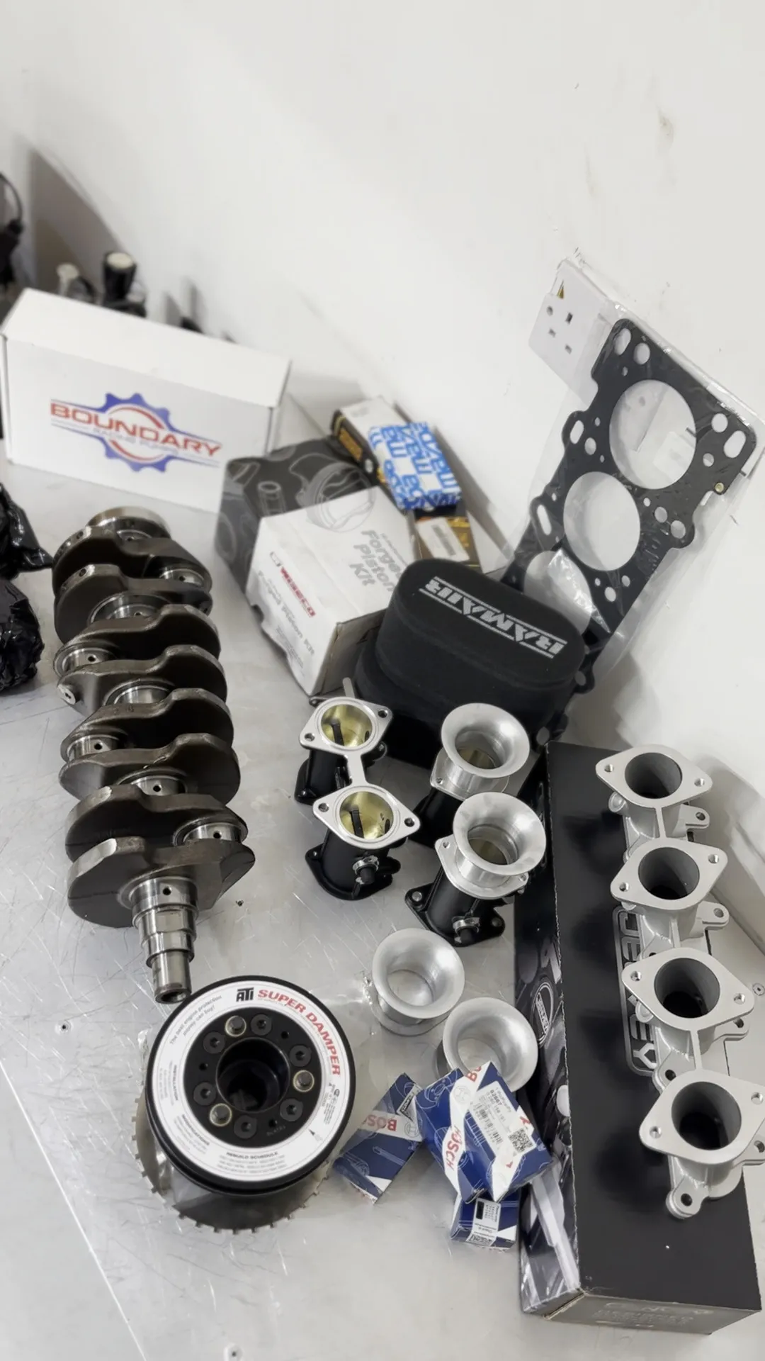 The full package on the bench, crank, boxed Wiseco pistons, the Boundary pump, damper, head gasket and inlet manifold