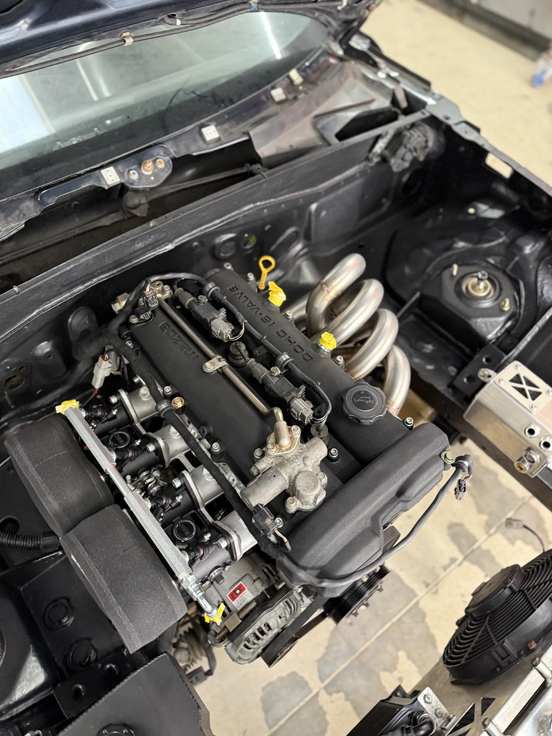 The four throttle bodies and trumpets in the engine bay, billet fuel rail above them and the green rocker cover behind