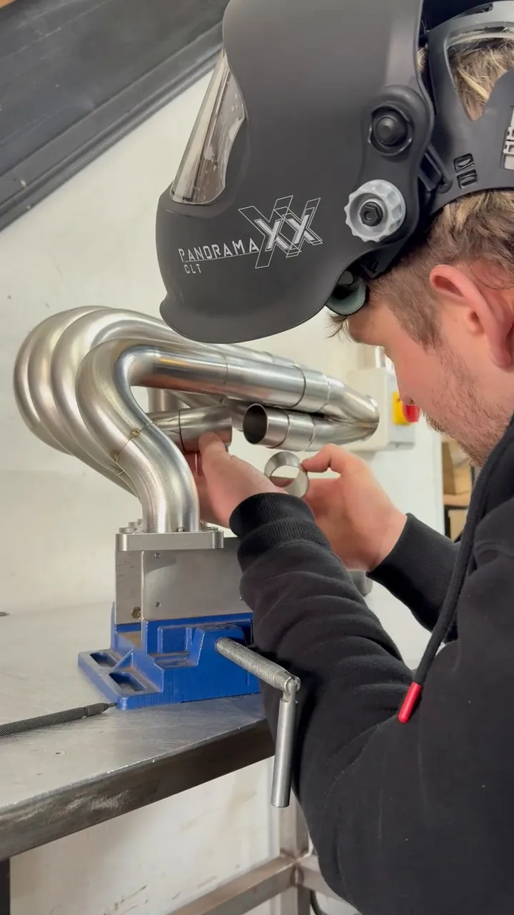 TIG welding a manifold joint on the bench, torch in hand and welding mask down