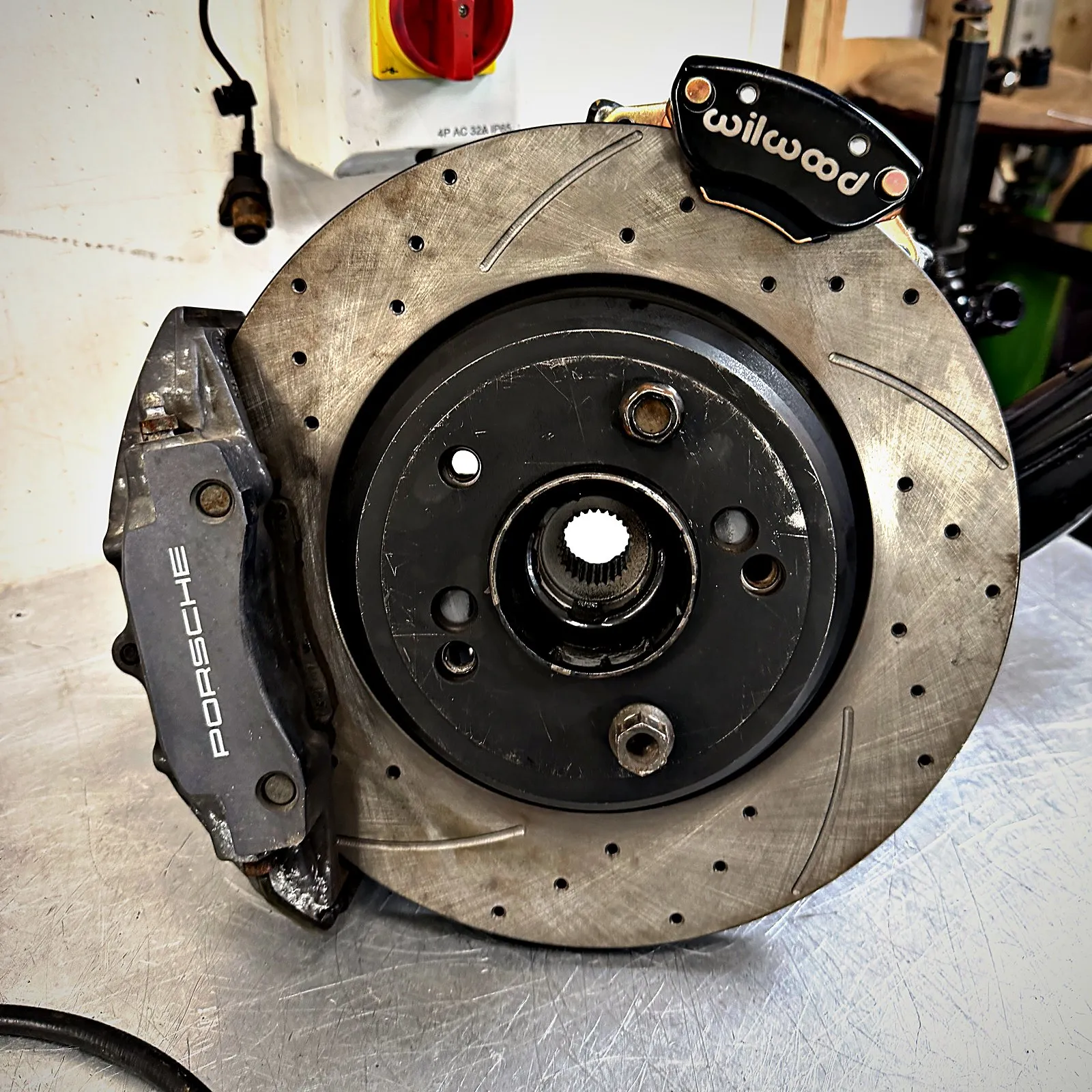 The kit built up on a rear hub: a Porsche caliper on a drilled and grooved disc, with a black Wilwood handbrake caliper on top