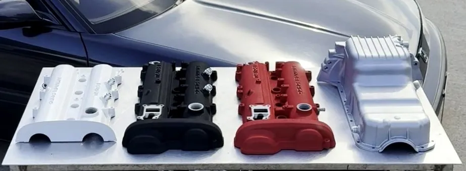 Finished rocker covers laid out on a bench, one white, one black and one red, beside a painted sump