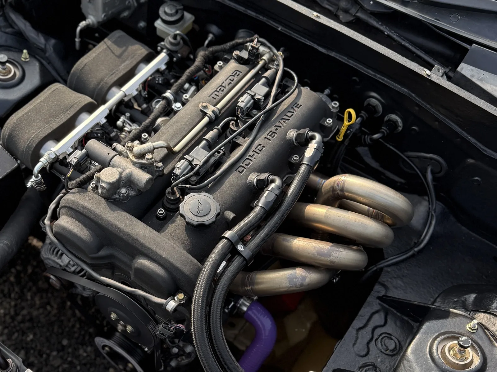 A fitted rocker cover on a turbocharged MX-5 engine, the braided breather lines running off its two AN10 fittings past the exhaust manifold