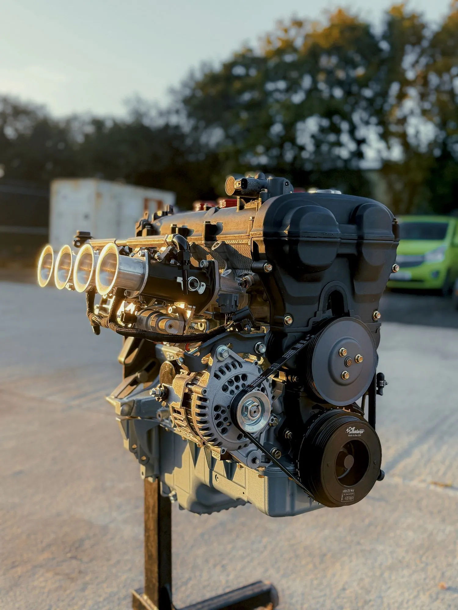A built MX-5 engine on the stand at golden hour, polished individual throttle bodies catching the light