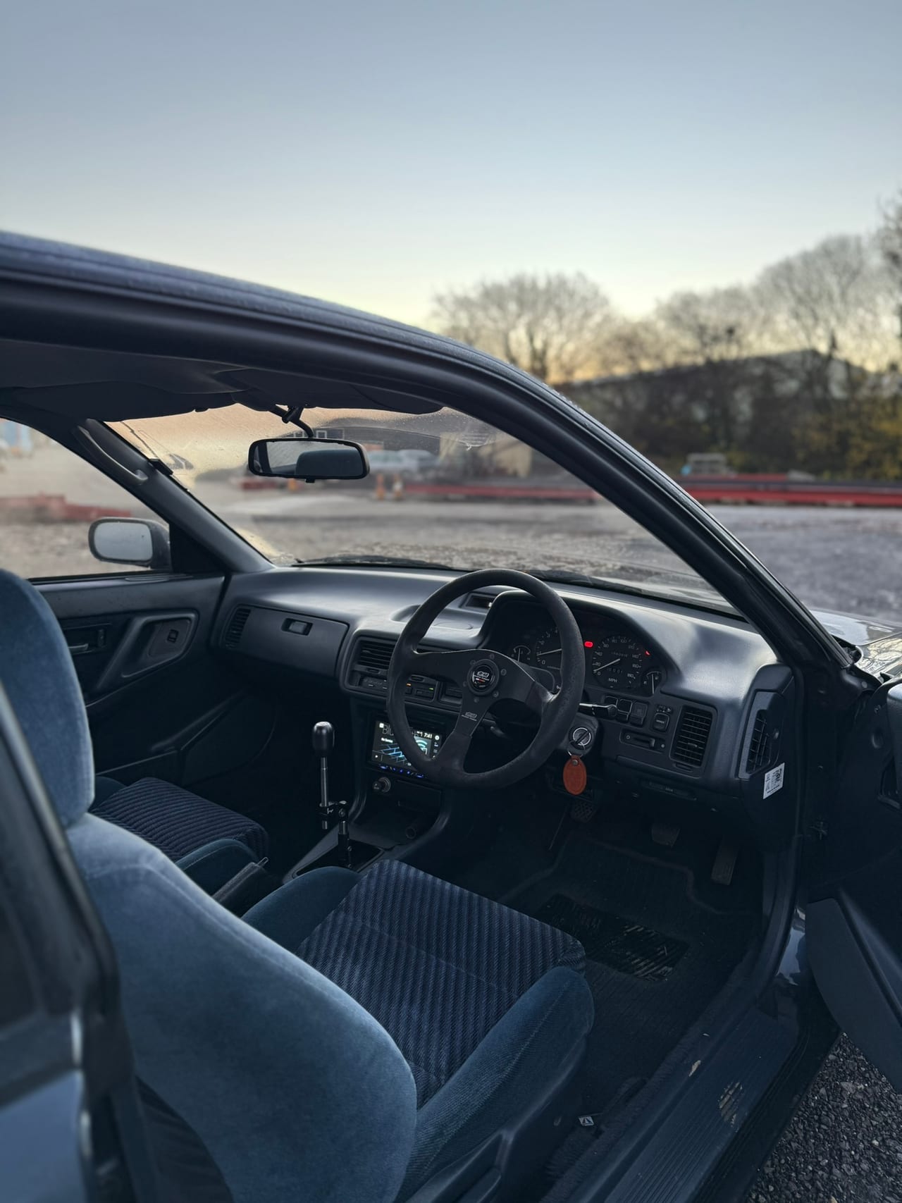 Inside a Honda Integra at the workshop, blue cloth interior and aftermarket wheel at dusk